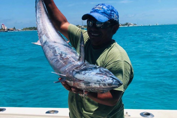 Person holding a large fish on a boat with blue ocean and sky in the background.